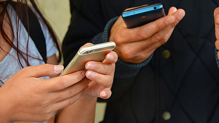 Ein Mann und eine Frau halten in ihren Händen jeweils ein Mobiltelefon.
