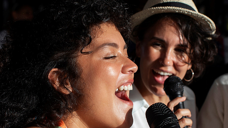 Das Bild zeigt zwei Frauen beim Singen mit einem Mikrofon.