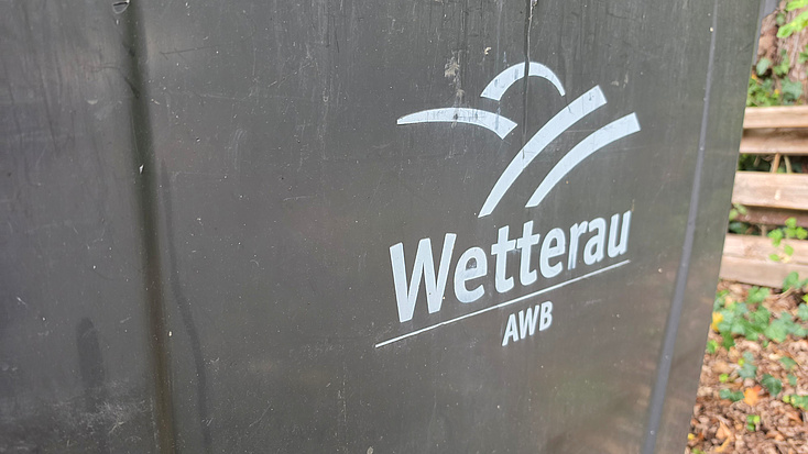 Eine Mülltonne mit der Aufschrift AWB und einem Logo steht im Freien.