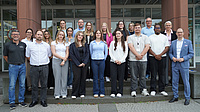 Mehrere Personen, vor allem Jüngere, stehen auf dem Stufen vor dem Eingang eines Bürogebäudes.