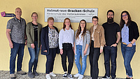 Acht Menschen stehen vor einem Schild, auf dem Helmut-von-Bracken-Schule steht.