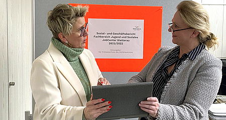 Zwei Frauen stehen sich gegenüber und halten gemeinsam eine Mappe in der Hand.