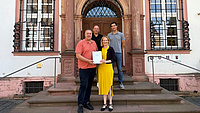 Vier Personen stehen auf der Treppe vor dem Niddataler Rathaus. Die beiden Personen im Vordergrund präsentieren eine Mappe mit dem Bescheid zur Dorfentwicklung in den Händen.