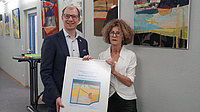 Zwei Menschen stehen vor einer Wand mit bunten Kuntswerken.