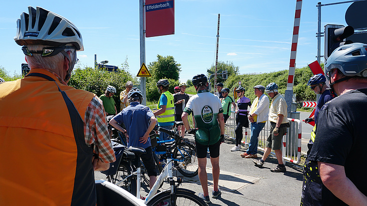 Eine Gruppe von Radfahrern steht vor dem Bahnübergang am Bahnhof Effolderbach.f