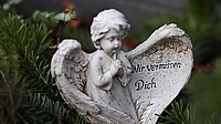 Ein Engel aus Stein, auf einem Flügel steht: "Wir vermissen dich"