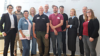 Vier Frauen und sieben Männer stehen in einem großen Saal vor einer Stellwand.