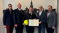 Fünf Männer stehen in einer Reihe. Der neue Kreisbrandmeister in der Mitte bekommt seine Urkunde überreicht.