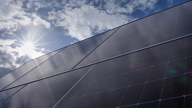 Photovoltaikmodule sind unter einem leicht bewölkten Himmel aufgestellt, von dem die Sonne scheint.