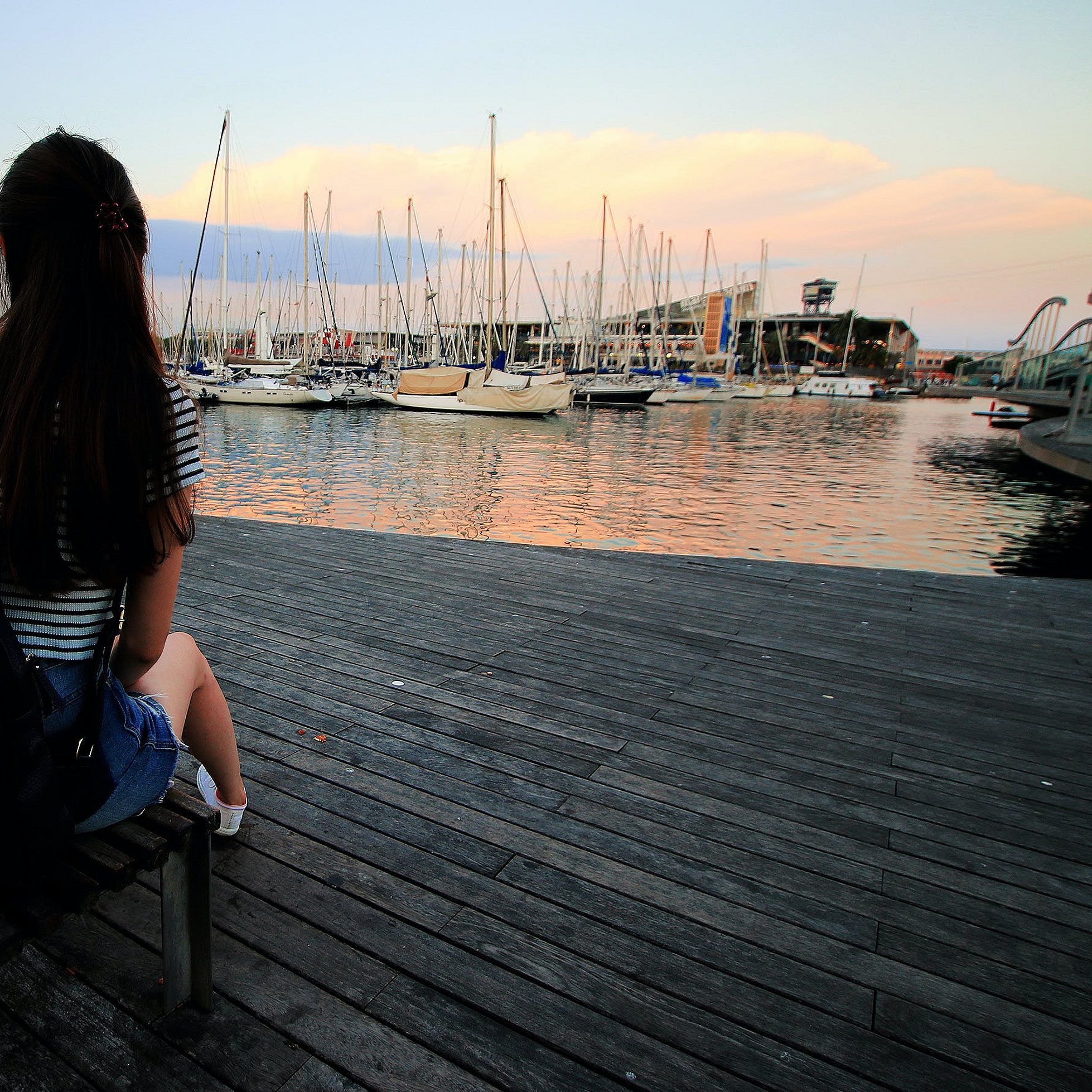 Ein Mädchen schaut von einem Steg aus aufs Wasser mit Booten